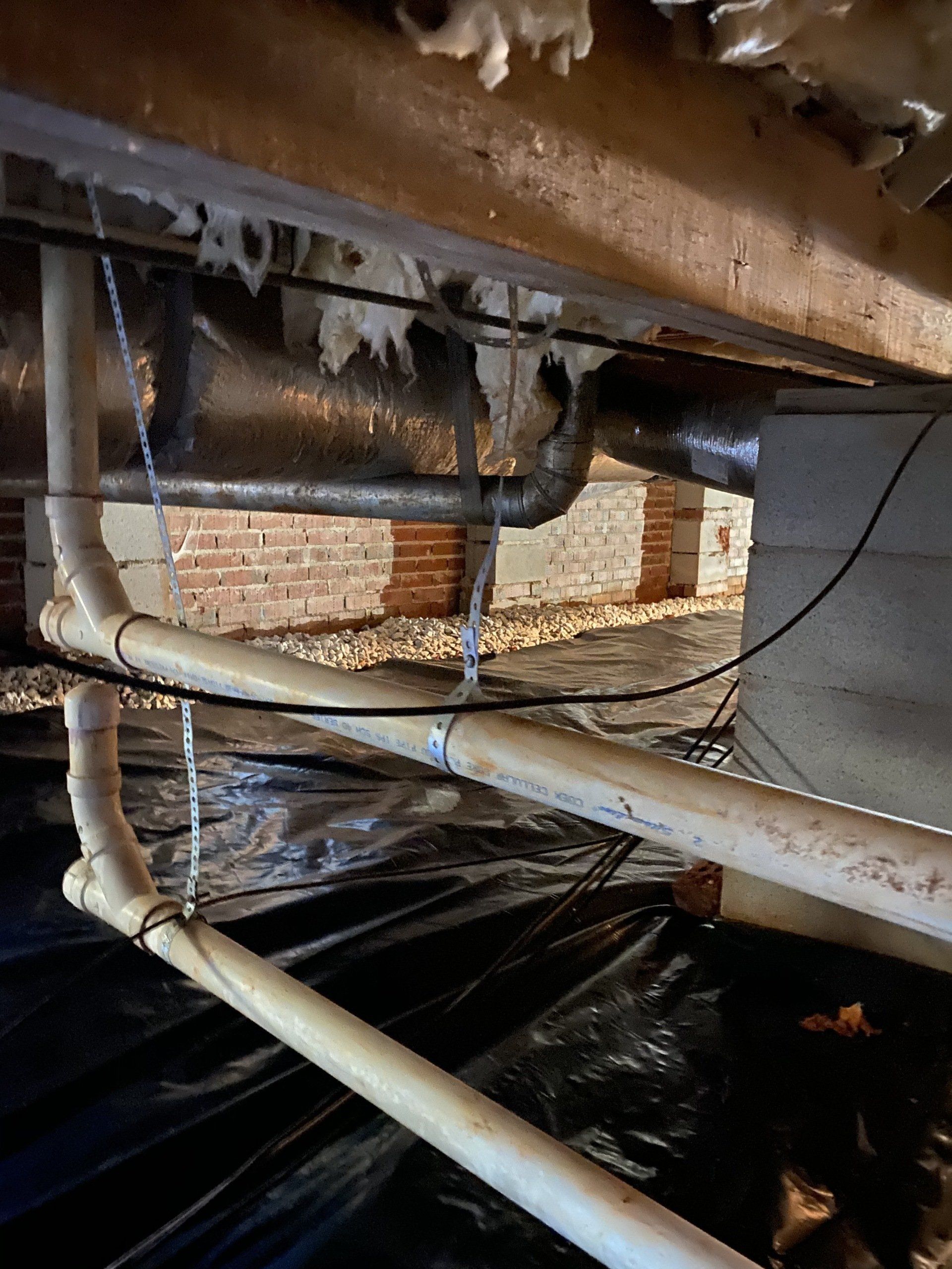 A bunch of pipes are hanging from the ceiling of a basement.