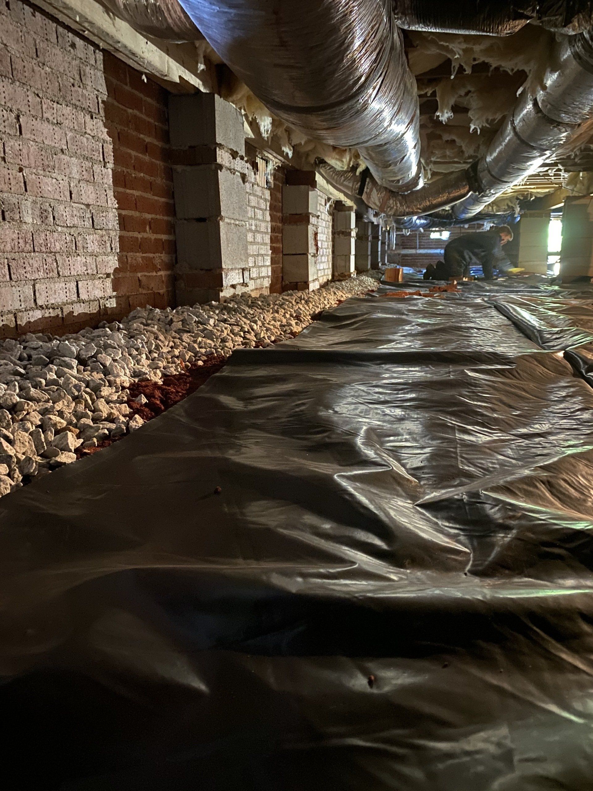 A crawl space with a lot of pipes and rocks in it.