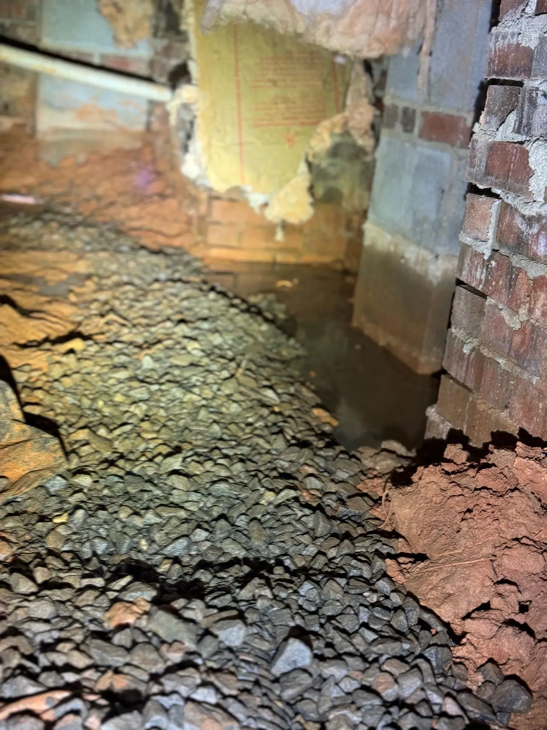 A close up of a brick wall and a rocky floor in a basement.