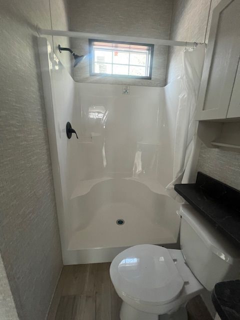 A bathroom with a toilet , shower and window.