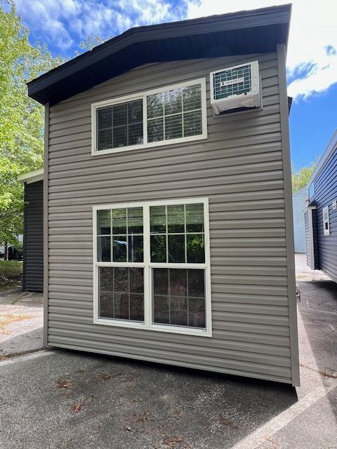 A small house with two windows and an air conditioner on the side of it.