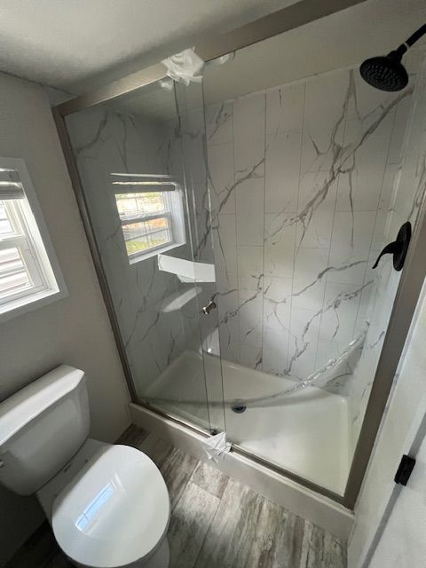 A bathroom with a toilet , shower and window.