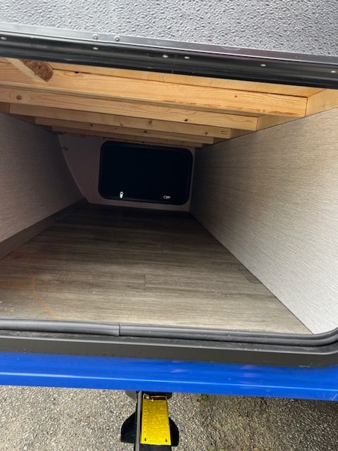 The inside of a trailer with a wooden floor and a window.