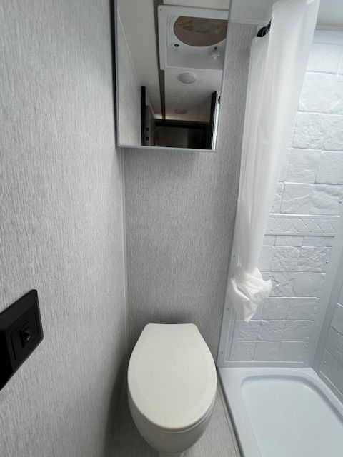 A bathroom with a toilet , shower and mirror.