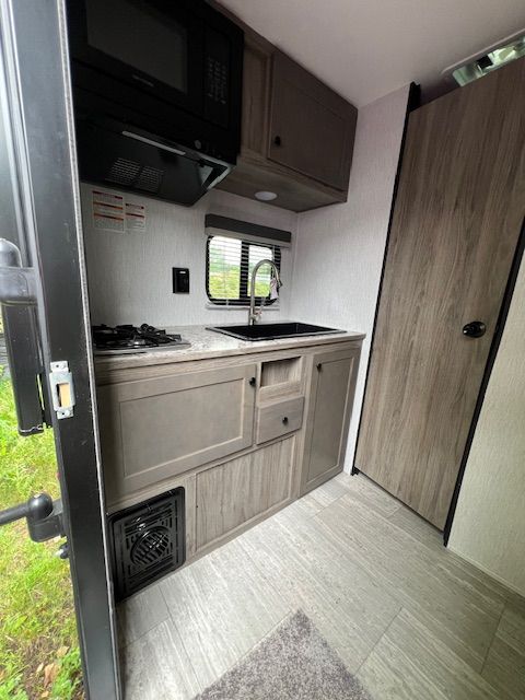 A small kitchen in a camper with a sink , stove and microwave.
