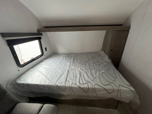 A bed with a mattress and a window in a trailer.