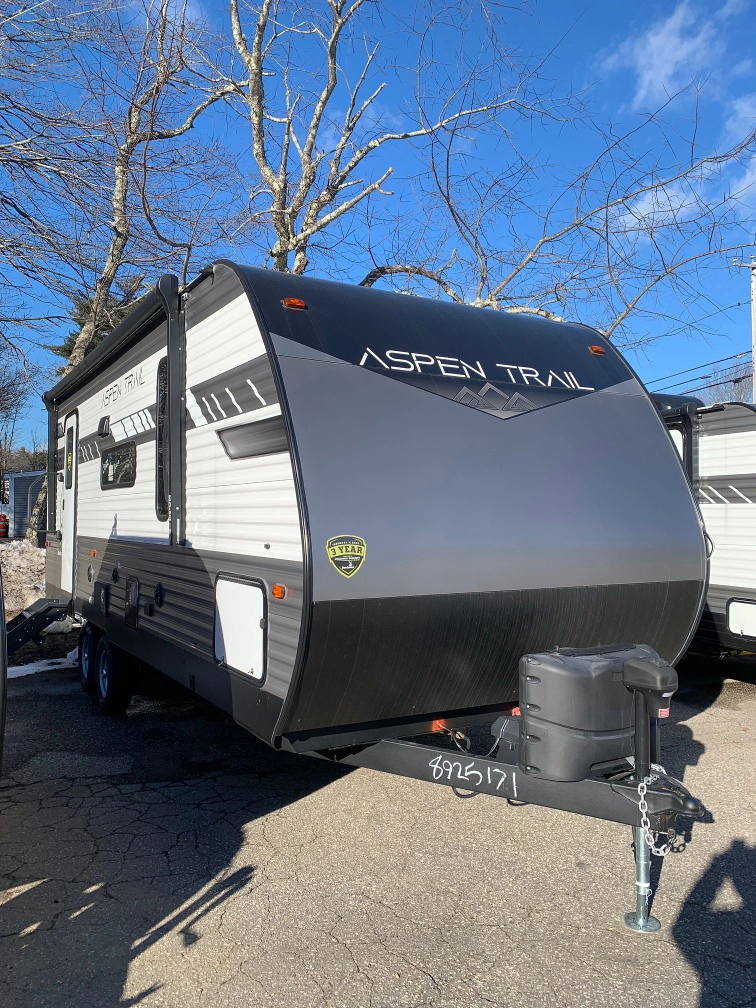 A black and white trailer is parked in a gravel lot.