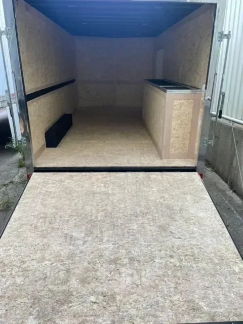 The inside of a trailer with the door open and a wooden floor.