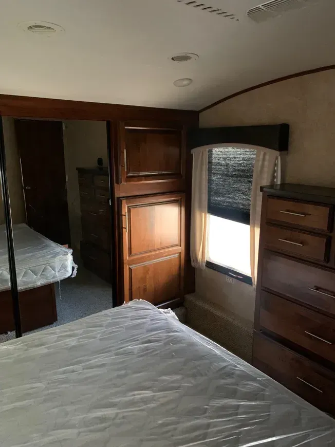 A bedroom with a bed , dresser , mirror and window.