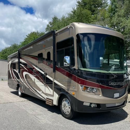 A large rv is parked in a parking lot with trees in the background