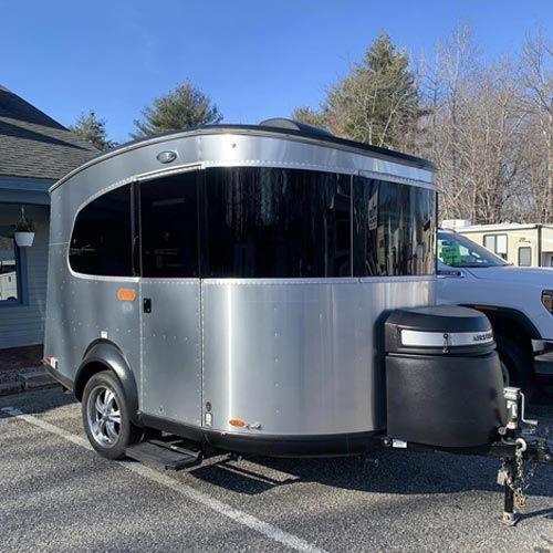 A silver trailer is parked in a parking lot next to a white truck.