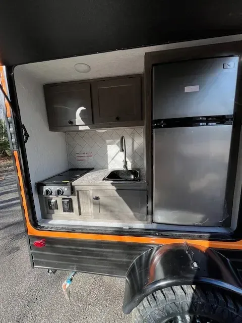 The inside of a trailer with a refrigerator , sink , and stove.