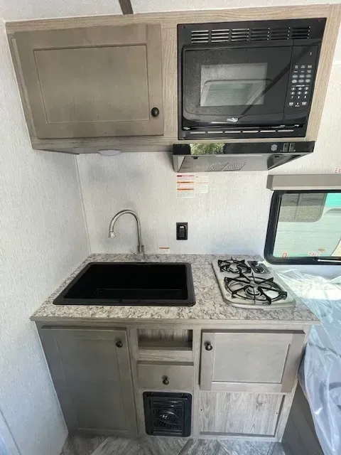 A kitchen in a camper with a sink , microwave , and stove.