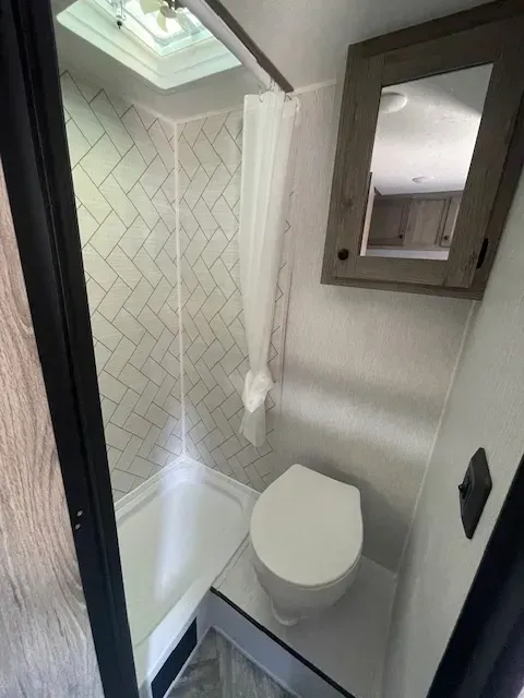 A bathroom with a toilet , shower and mirror.