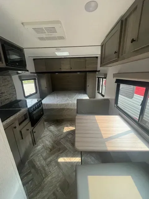 The inside of a rv with a bed , table , and stove.