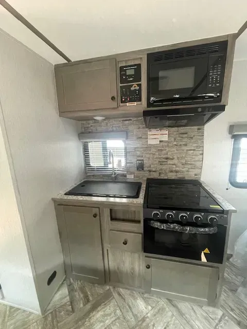 A kitchen in a rv with a stove , microwave and sink.