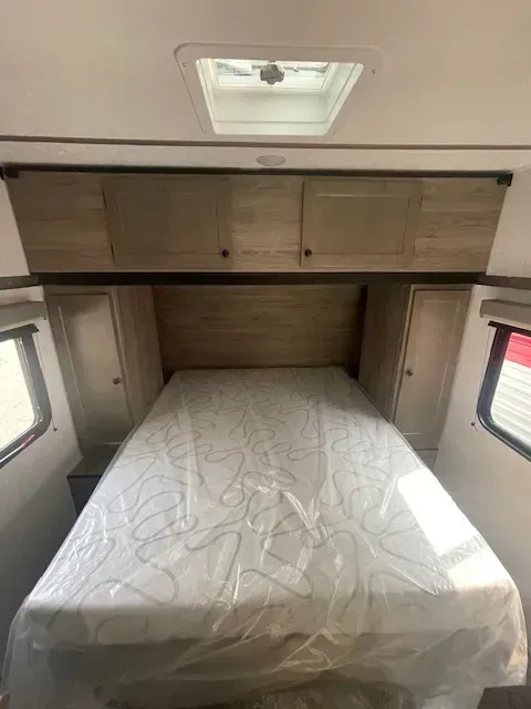 A bed in a trailer with a mattress and cabinets.