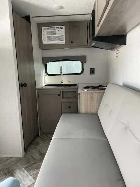 A rv with a couch , sink , cabinets and a window.