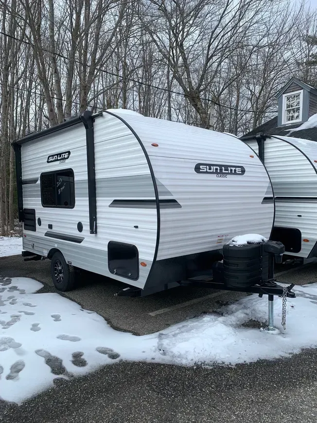 A small white trailer is parked in a snowy parking lot.