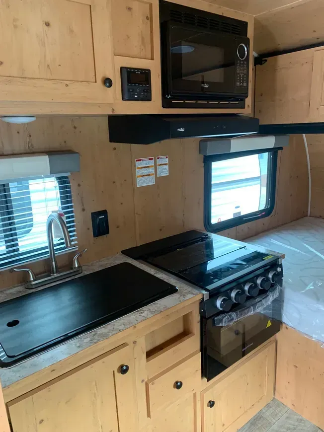 A kitchen in a camper with a sink , stove , microwave and a bed.