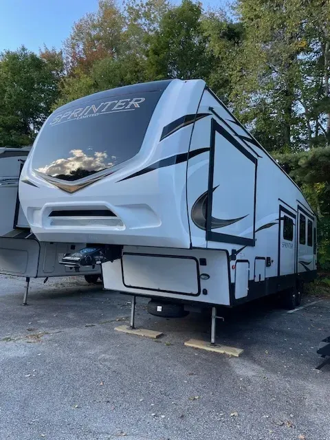A white rv is parked in a parking lot with trees in the background.