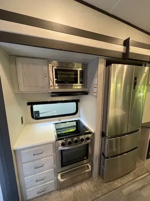 A kitchen in a rv with a stove , refrigerator and microwave.