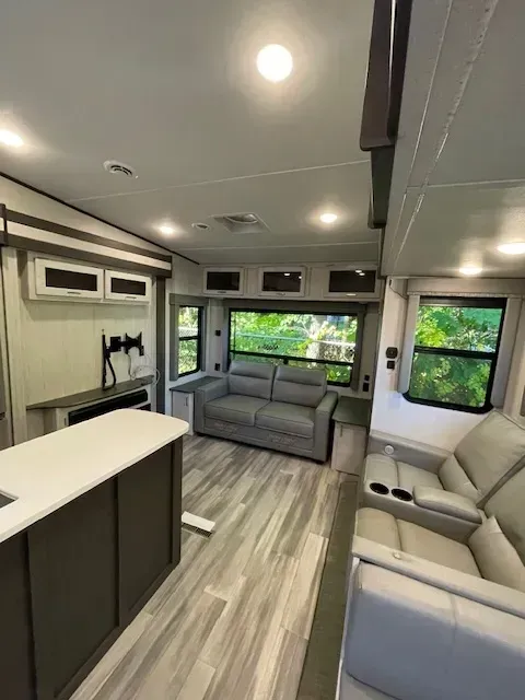 A living room in a rv with a couch , chairs , and a kitchen.
