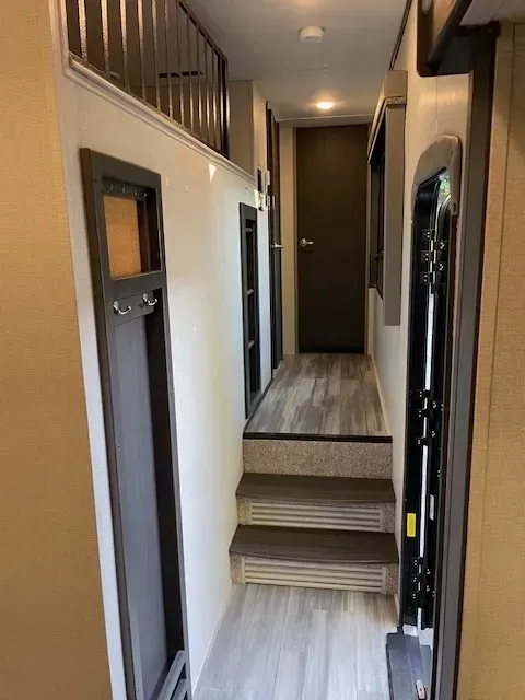 A hallway with stairs leading up to a door and a window.