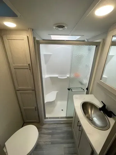 A bathroom with a toilet , sink , shower and mirror.