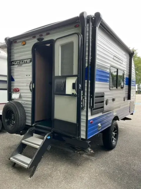 A blue and white trailer with stairs is parked in a parking lot.