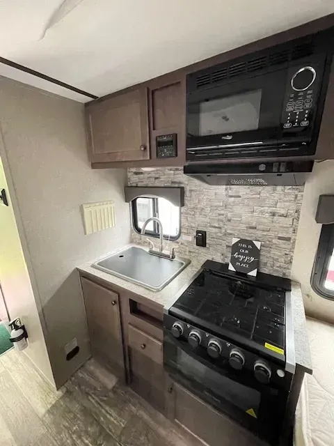 A kitchen in a rv with a sink , stove and microwave.
