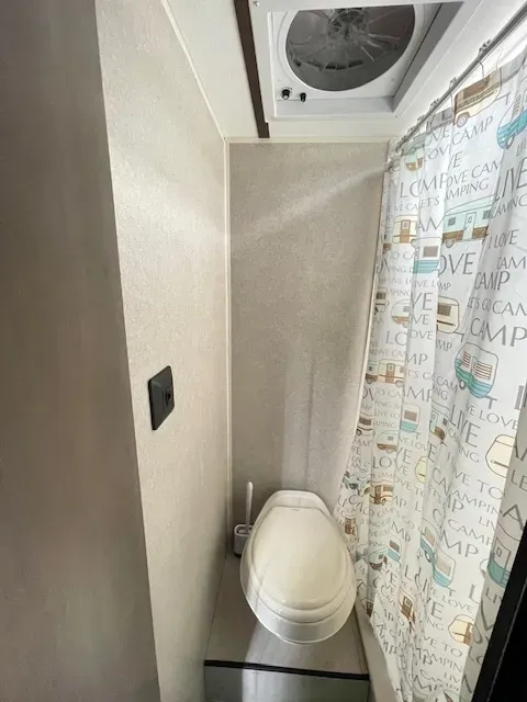 A bathroom with a toilet , shower curtain and fan.