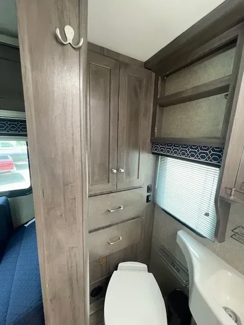A bathroom in a rv with a toilet , sink and cabinets.