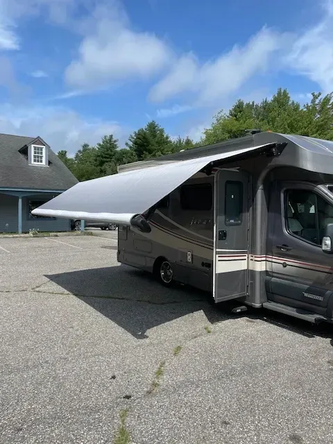 A rv with an awning is parked in a parking lot