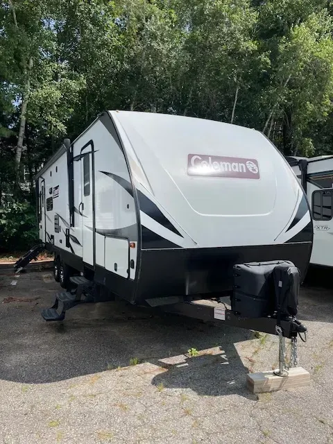 A white and black coleman trailer is parked in a parking lot.