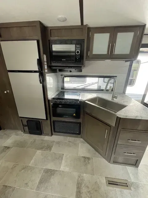 A kitchen in a rv with a refrigerator , microwave , sink and stove.