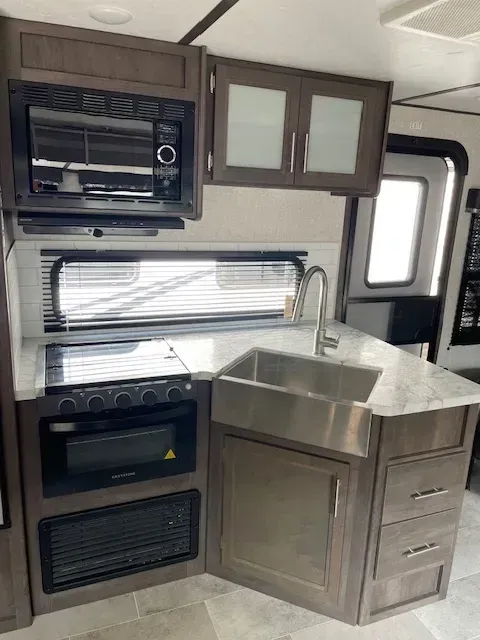 A kitchen in a rv with a sink , stove , microwave and oven.
