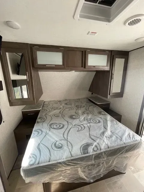 A bed in a trailer with a mattress wrapped in plastic.