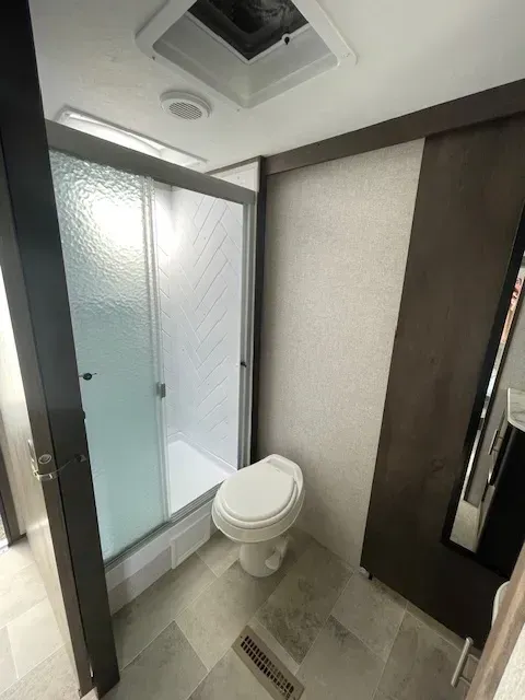 A bathroom with a toilet , shower and mirror.