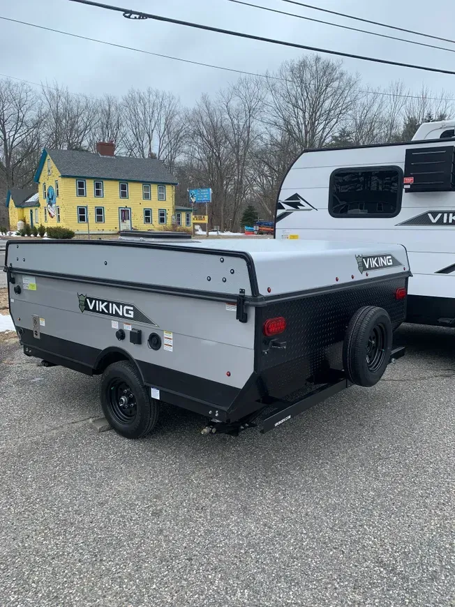 A viking trailer is parked next to a rv in a parking lot.