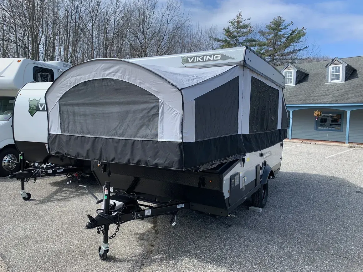 A camper trailer is parked in a gravel lot in front of a house.