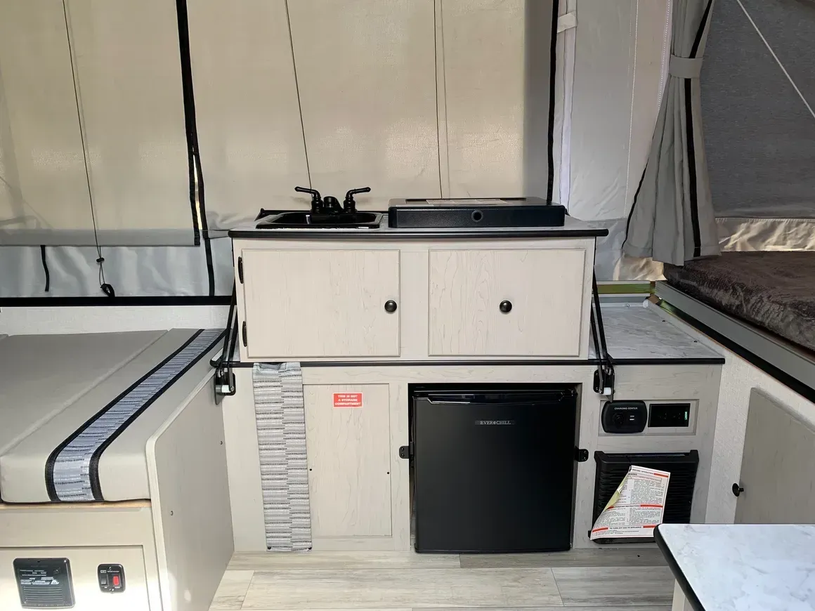 A kitchen in a camper with a sink , refrigerator , and cabinets.