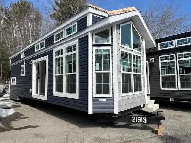 A tiny house with a lot of windows is parked in a parking lot.