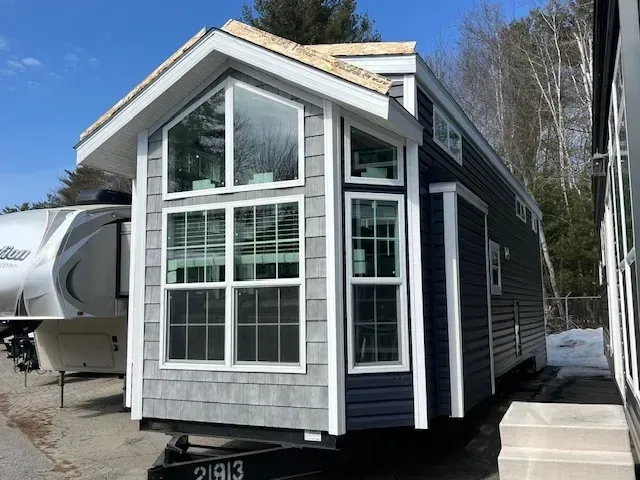 A small house with a lot of windows is parked next to a trailer.