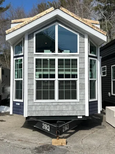 A small house with a trailer attached to it is sitting on the side of the road.