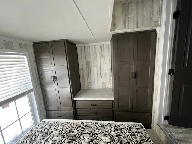 A bedroom with a bed , cabinets , drawers and a window.