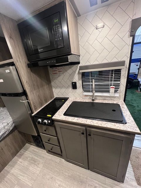 A kitchen in an RV with a sink, stove, microwave, and refrigerator.