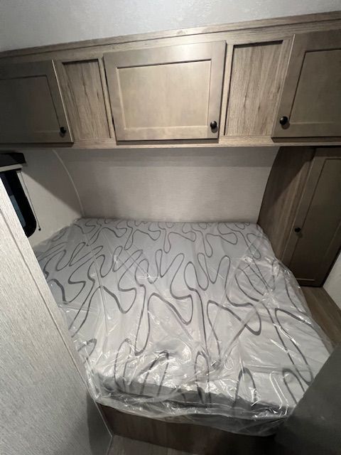 A bed in a trailer with a mattress and cabinets.