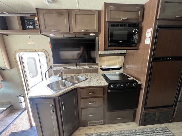 A kitchen with a sink, stove, microwave, and refrigerator