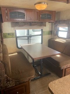 Interior of a camper with a table, two benches, cabinets, and a window.